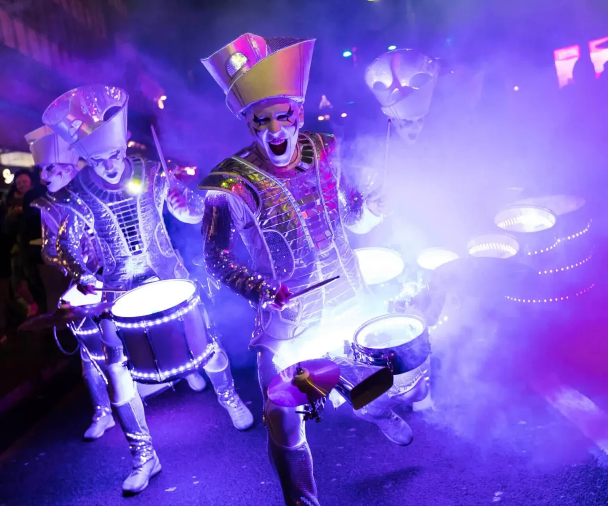 Spark! performers drumming through purple smoke at a night festival, drums glowing.