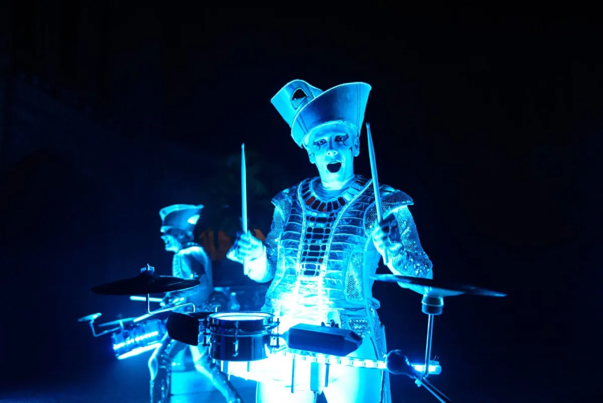 A Spark! performer drumming in electric blue light at a corporate party, a second drummer behind.