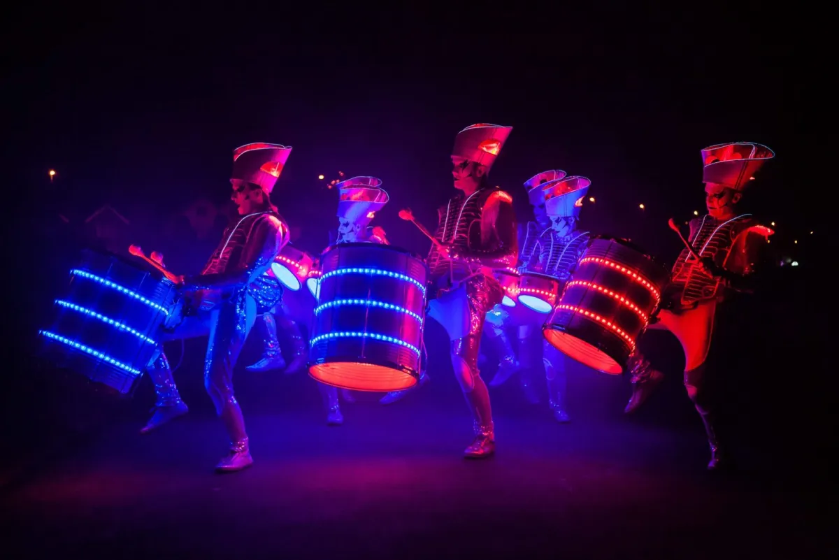 Five Spark! performers drumming in the dark, drums banded red, blue and orange.