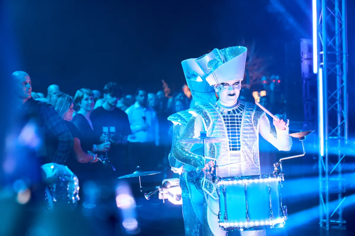A Spark! performer drumming in blue light at a company Christmas party, guests behind.
