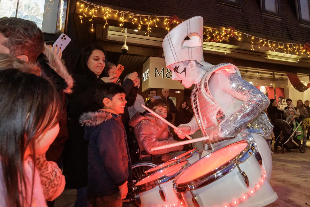 A Spark! performer leaning in as a child plays the illuminated drums, families watching under Christmas lights.