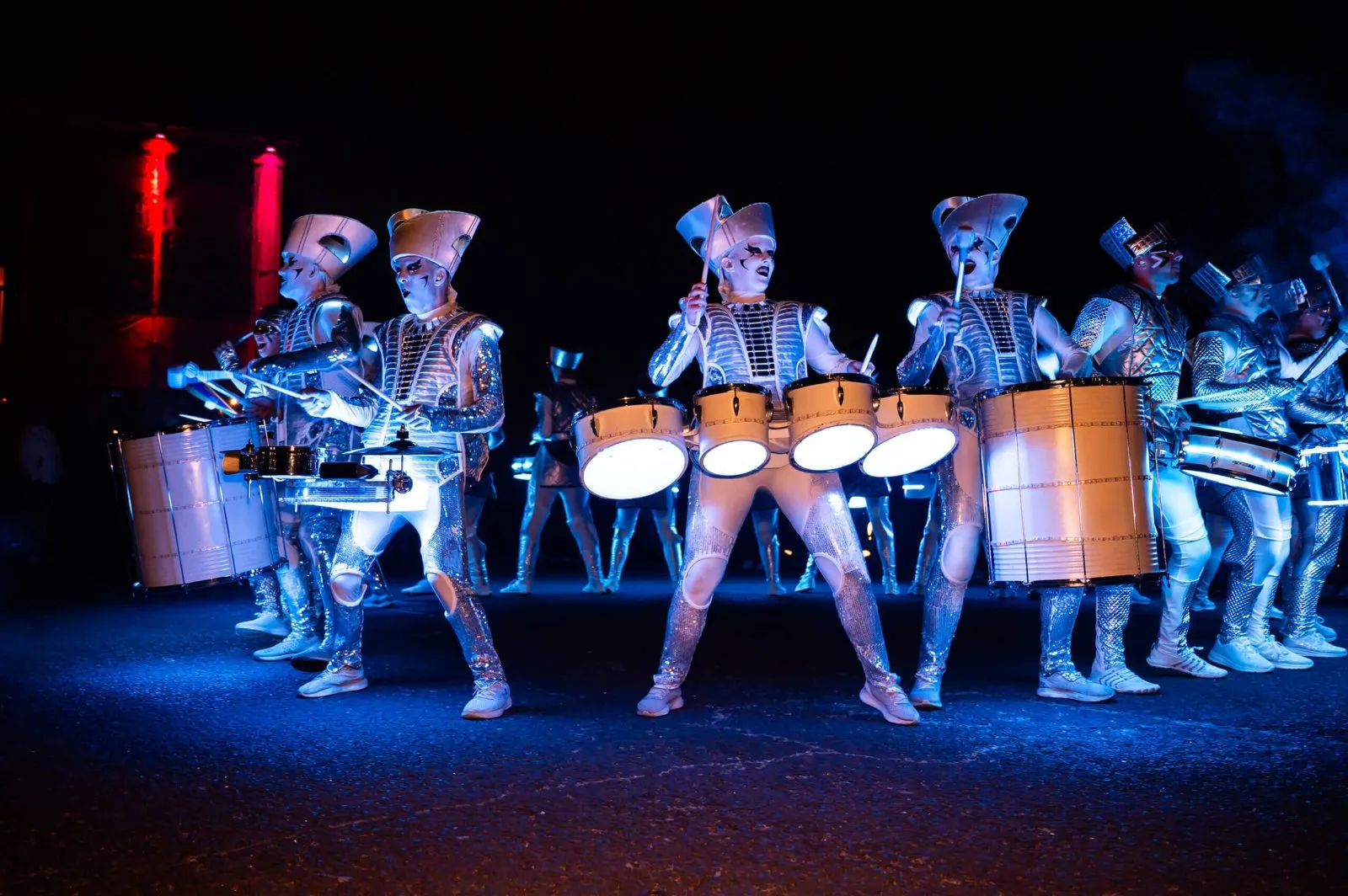 The combined Spark! and Fireflies ensemble drumming together, drums glowing white and blue.
