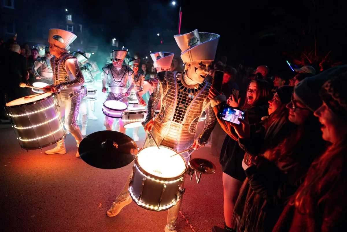 Fireflies performers drumming close to a delighted street crowd at night.
