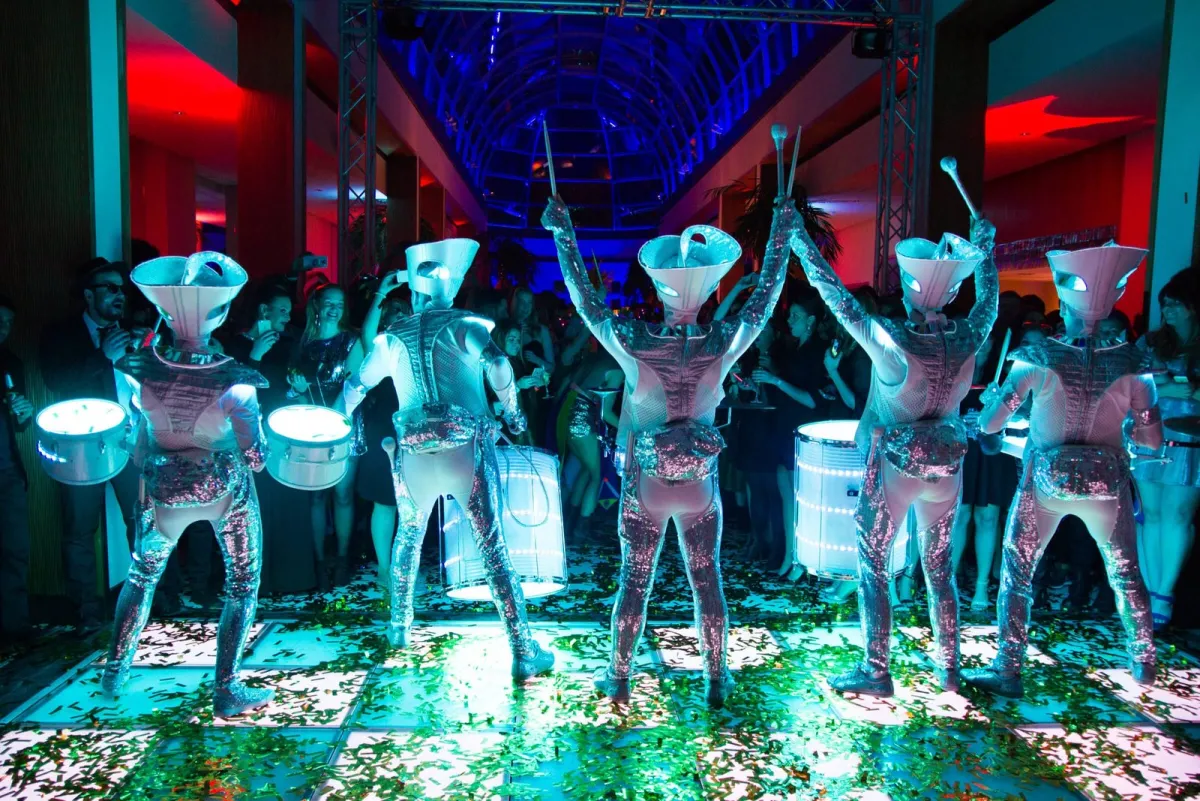 Spark! performers arms aloft on a confetti-covered dance floor at an indoor party.
