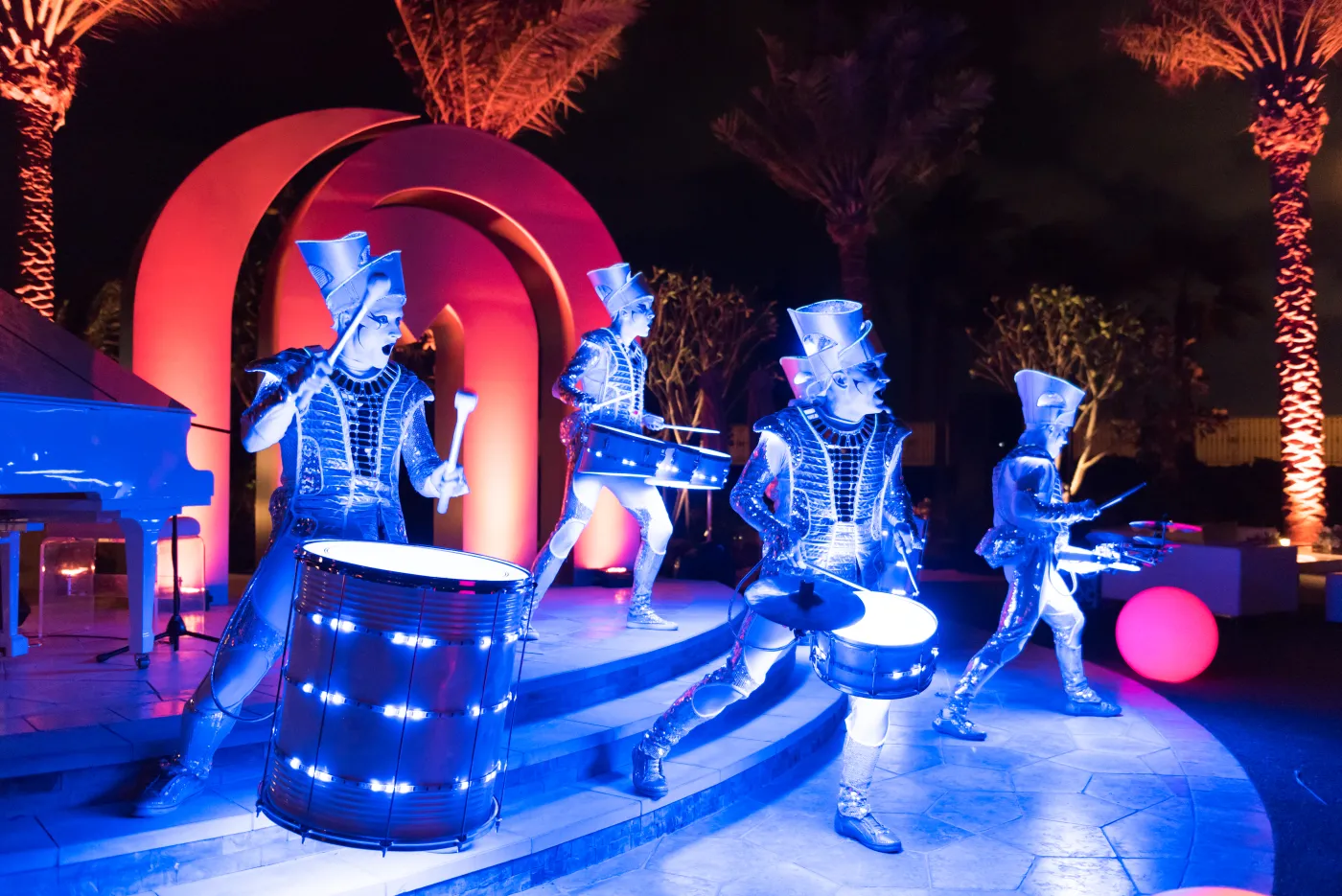 Spark! performers lit electric blue on an outdoor stage framed by illuminated arches and palm trees at a Gulf event.