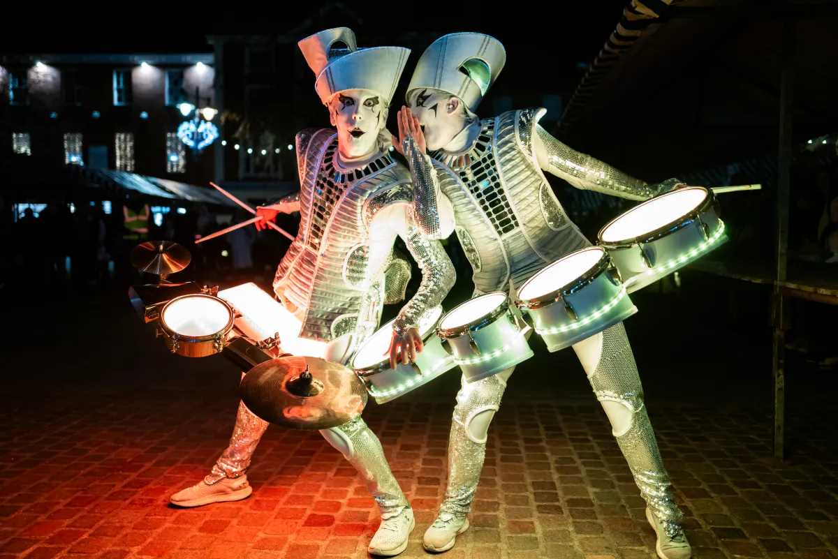 Two Spark! performers in handmade illuminated costumes, their drums glowing warm orange.