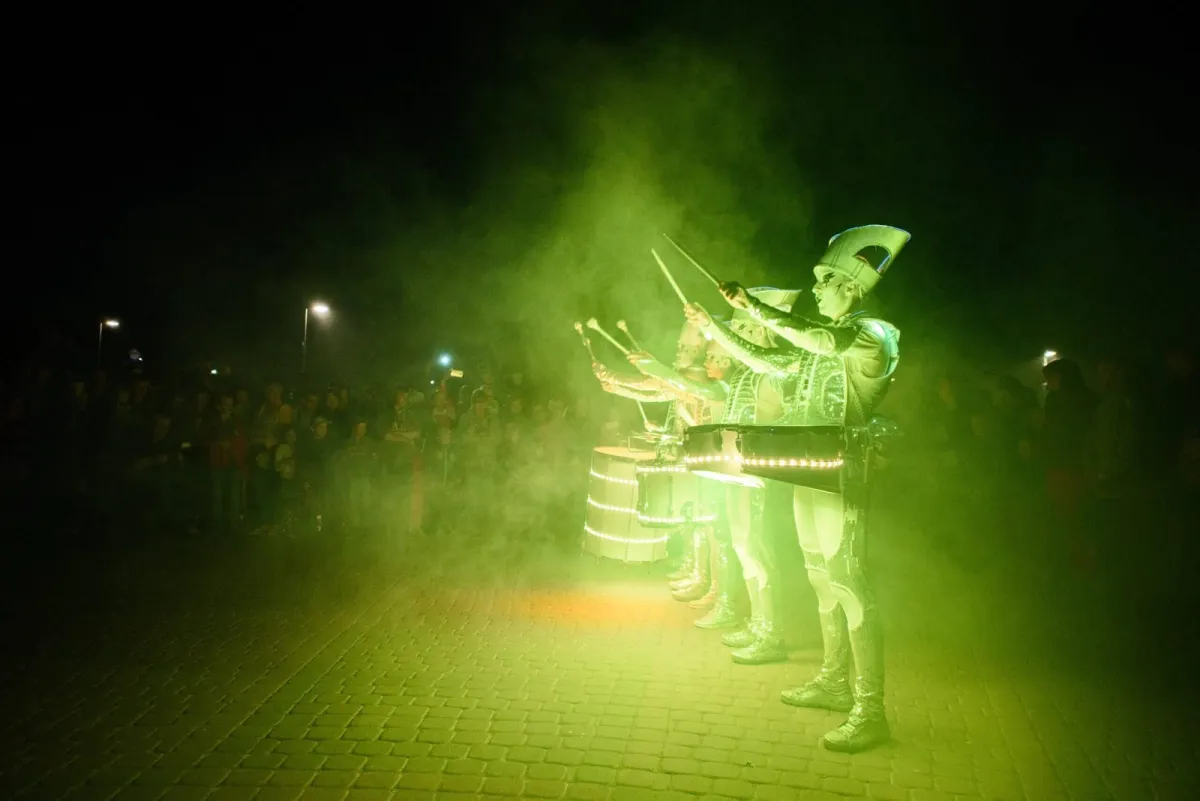 Spark! performers drumming in dramatic green light and smoke as a crowd watches.