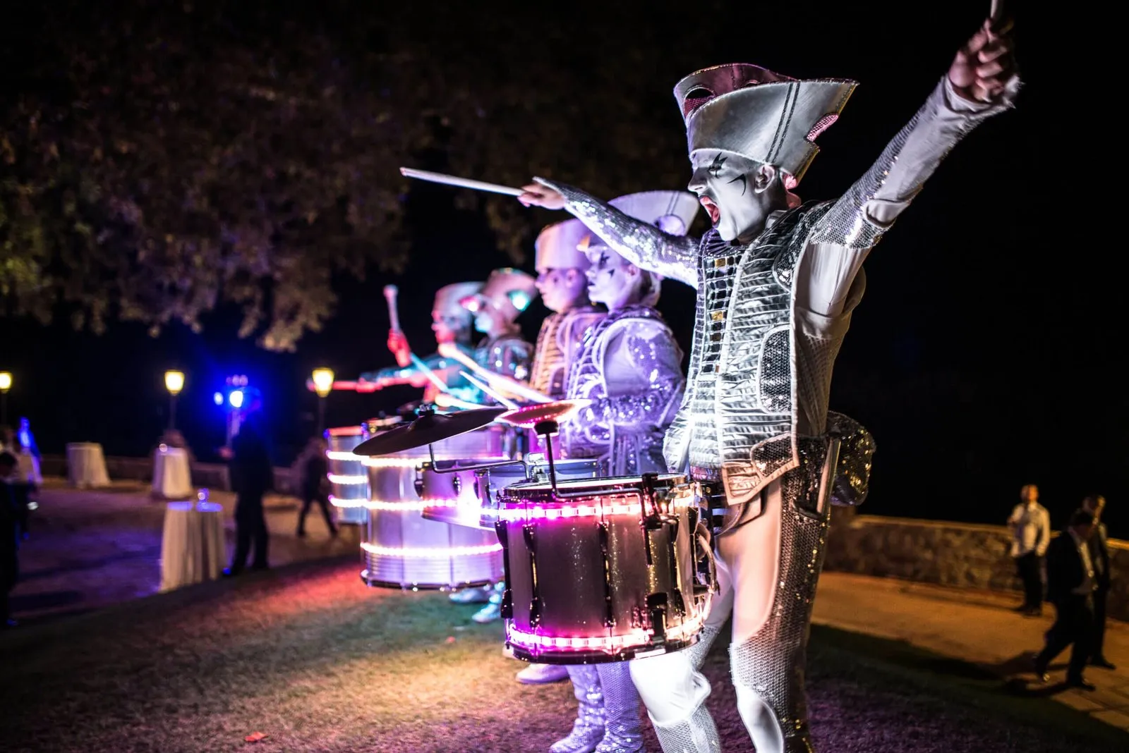 Spark! performers drumming at an elegant outdoor corporate event, guests at candlelit tables behind.