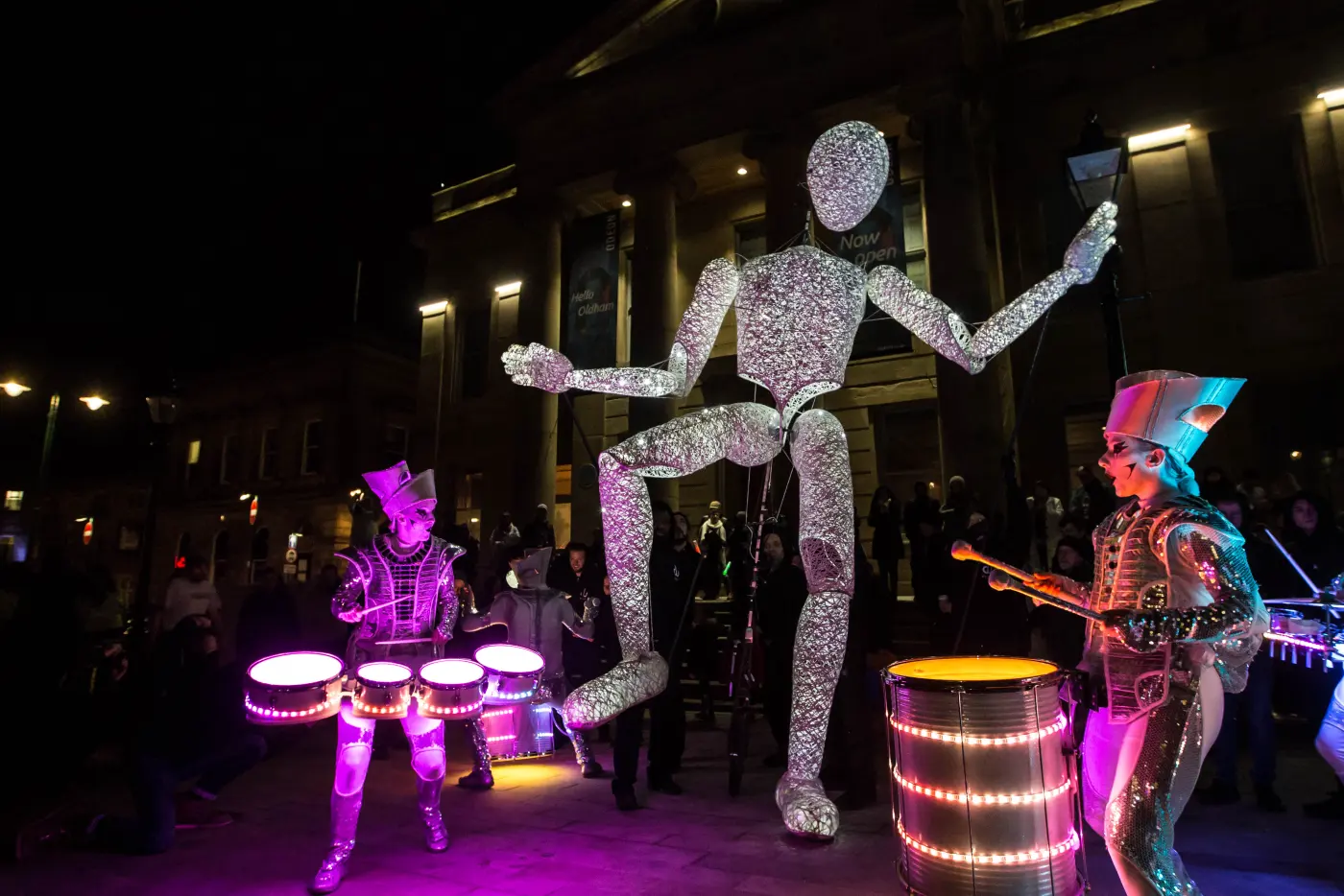 Dundu dancing between Spark! drummers on pink and gold drums in Oldham's Parliament Square.