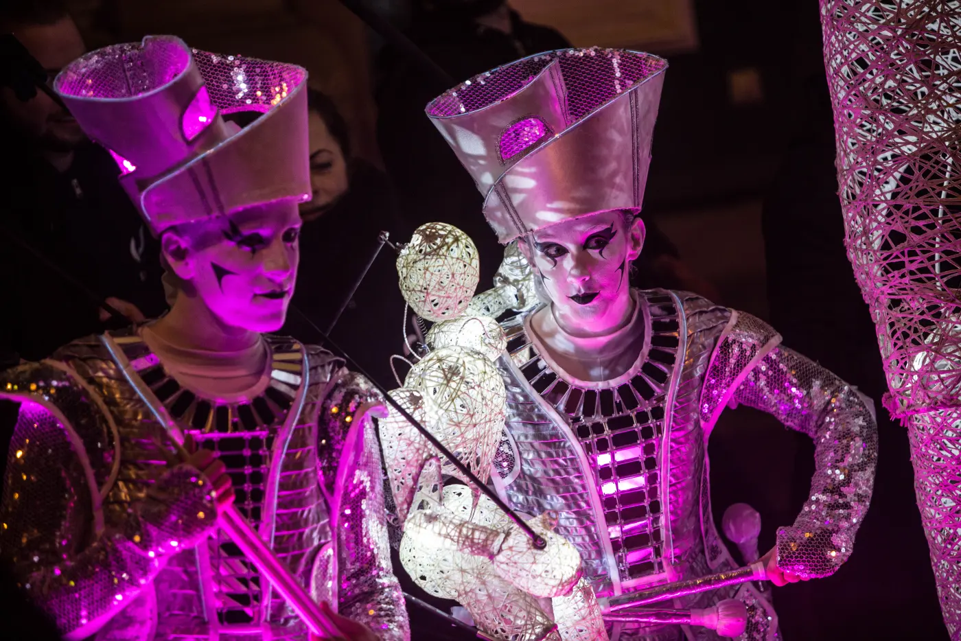 Two Spark! performers lit magenta, with Baby Dundu perched between them, at Illuminate Oldham.