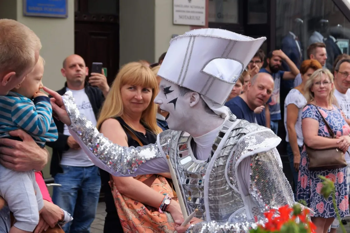 A Spark! performer in silver costume greeting a toddler in a daytime street crowd.