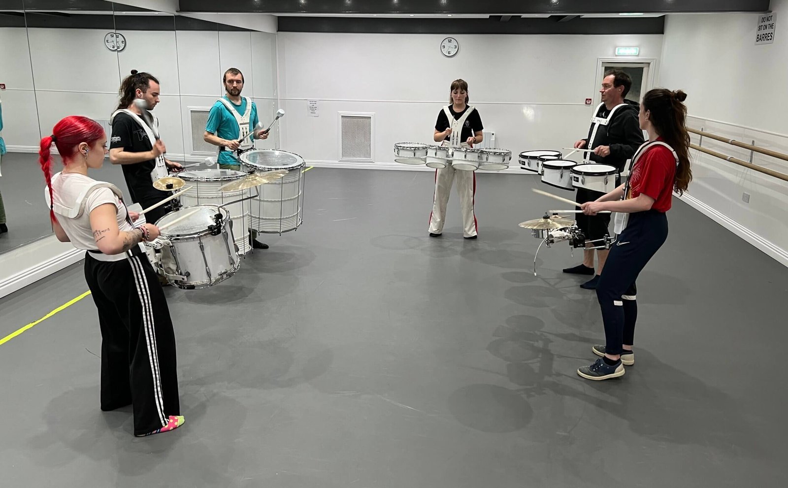 Six new performers learning drum parts in a rehearsal studio