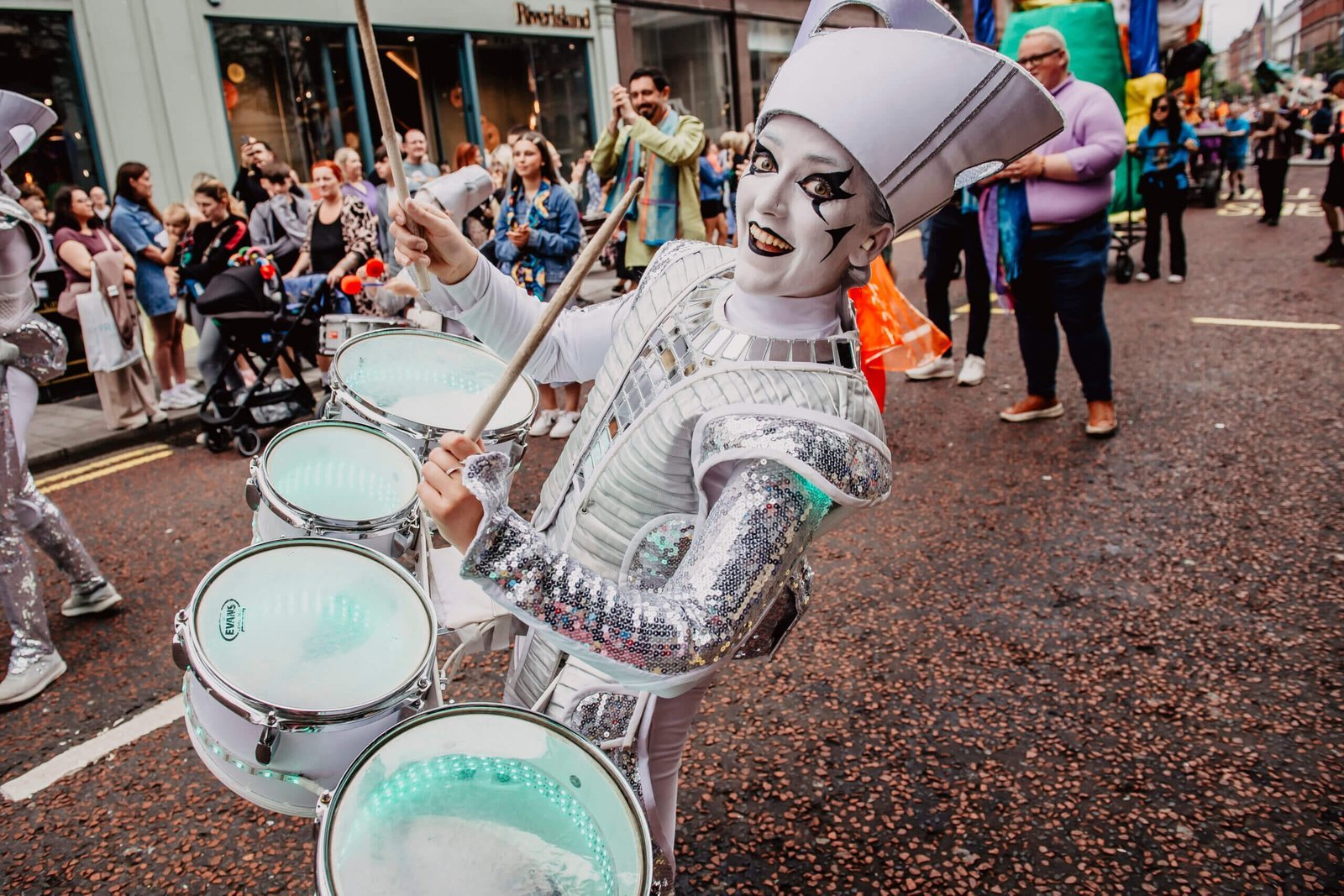 A Spark! performer drumming through a packed daytime carnival crowd