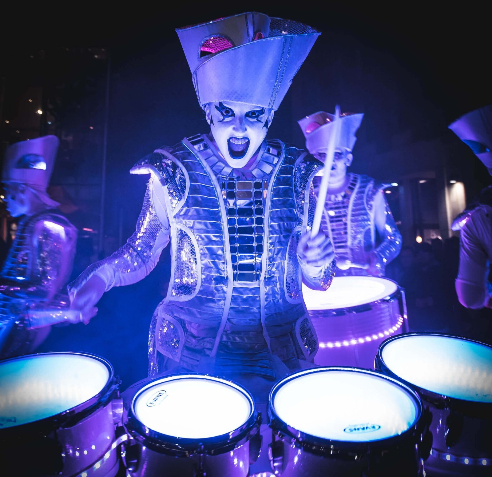 A Spark! performer mid-roar over glowing illuminated drums at night