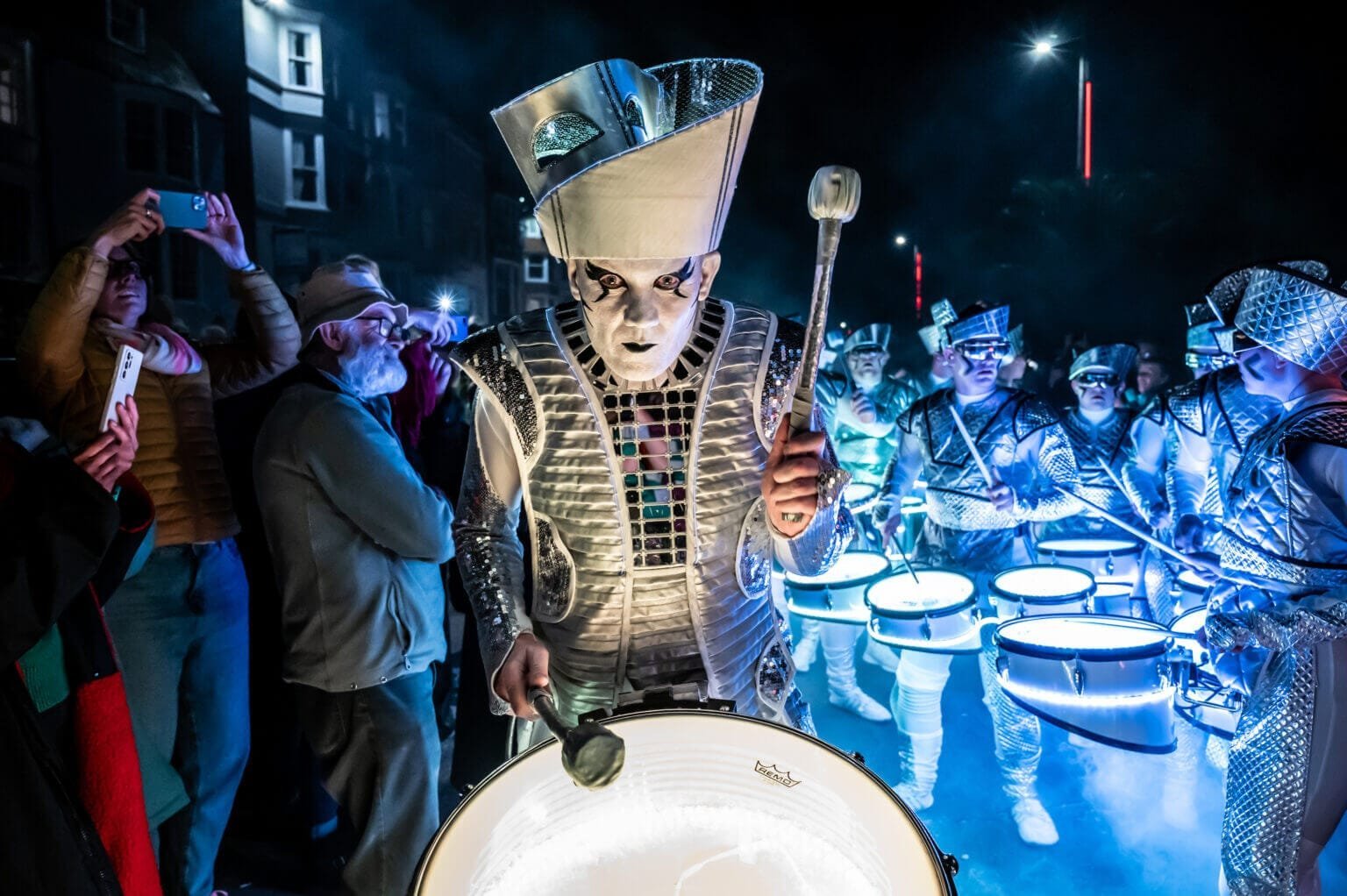 A night-time crowd filming as a Spark! drummer performs up close