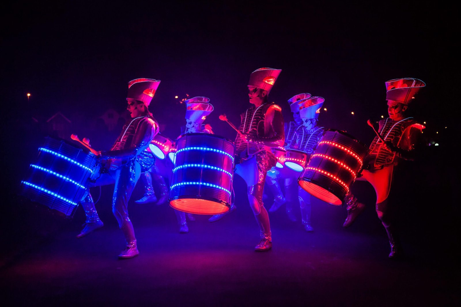 Five Spark! performers in a line at night, illuminated drums glowing blue and red